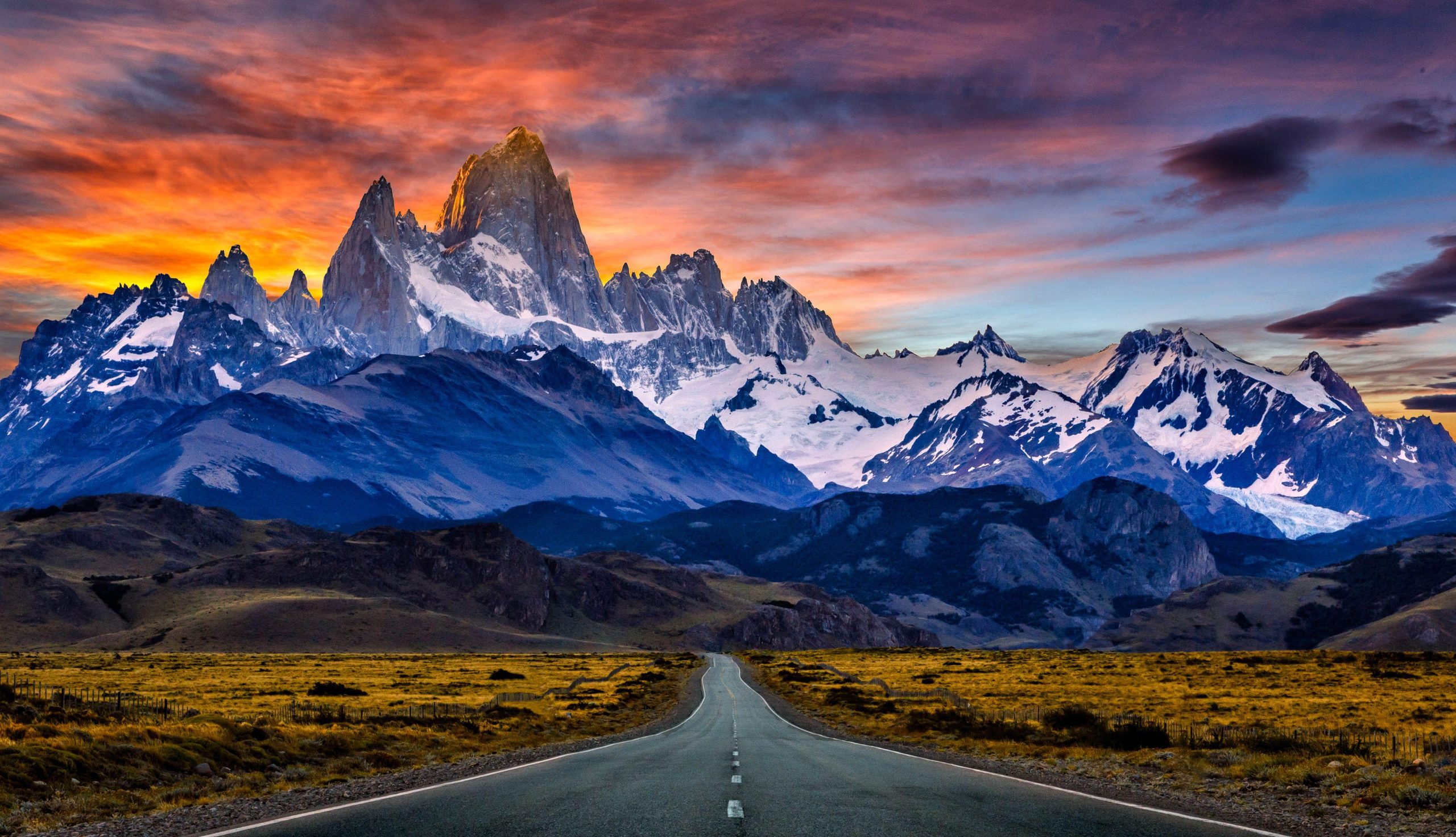 A road running towards a snow-capped mountain range at sunrise